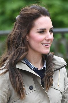 a woman with long hair wearing a trench coat and smiling at someone in the distance