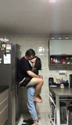 a man and woman hug in the kitchen while standing next to each other on top of a refrigerator