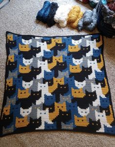 a crocheted blanket with cats on it and balls of yarn next to it