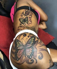 a woman laying on her stomach with butterfly tattoos on her back and legs, both showing