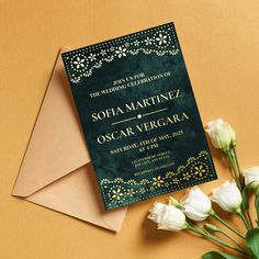 a green and gold wedding card on top of an envelope with white flowers in it