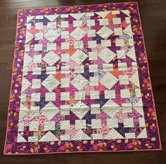 a purple and pink quilt on a wooden floor