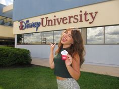 a woman holding up a candy bar in front of a disney university sign and building