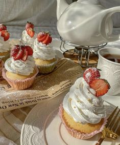 cupcakes with whipped cream and strawberries sit on plates next to a tea kettle