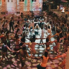 a large group of people are dancing on the floor in front of an old building