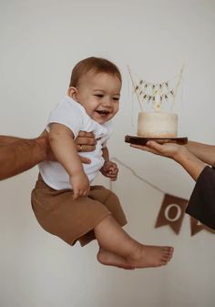 a baby is being held up in the air by two adults and holding a cake