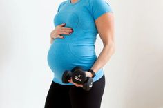 a pregnant woman holding two black dumbs