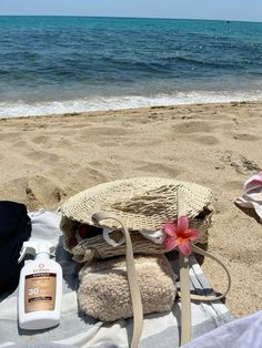 a bottle of sunscreen, towel and hat on the sand at the beach near the ocean