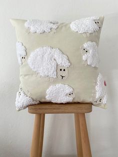 a pillow with white sheep on it sitting on a wooden stool next to a wall