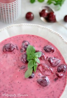 a white plate topped with a bowl filled with berries and cream sauce next to fresh cherries