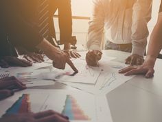 several people standing around a table with papers and pencils on it, pointing at graphs