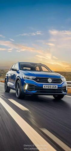 a blue volkswagen suv driving down the road at sunset or dawn with clouds in the background