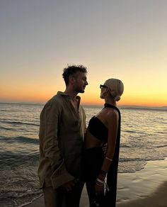 a man and woman standing on the beach at sunset