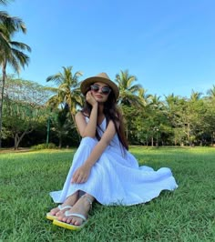 a woman sitting on the grass wearing sunglasses and a hat