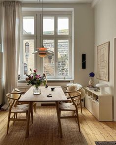 a dining room table and chairs in front of a window with flowers on the table