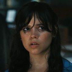 a woman with long black hair and blue shirt looking off to the side while standing in front of a building