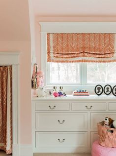 a white dresser topped with lots of drawers next to a window covered in pink curtains