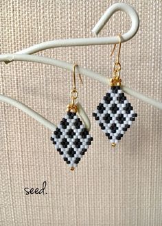 black and white beaded earrings hanging from a hook on a wall with the words seed written in gold