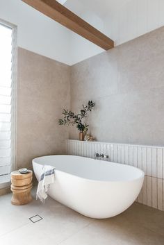 a white bath tub sitting in a bathroom next to a wooden stand with a potted plant on it