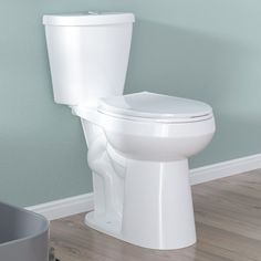 a white toilet sitting on top of a wooden floor next to a gray trash can