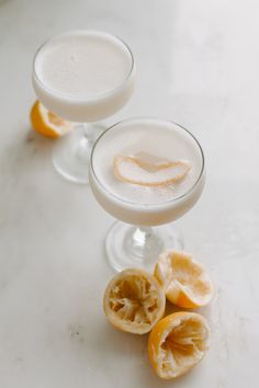 two glasses filled with drinks sitting on top of a white counter next to sliced oranges