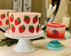 two cakes with strawberries on them sitting on a table next to another cake that has strawberrys on it