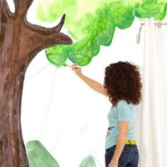 a woman is painting a tree on the wall