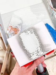 a person using a paint brush to spray paint on a piece of paper with silver sequins