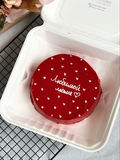 a red cake with white hearts on it in a plastic container next to a flower