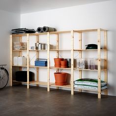 a shelf with pots, books and other items on it in front of a white wall