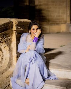 a woman in a blue dress sitting on the steps with her hand to her face