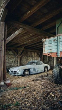 an old car is parked in the barn next to a truck and tractor tire on the ground