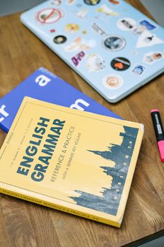 two books sitting on top of a wooden table next to a pink pen and marker