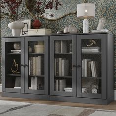 a black bookcase with glass doors in front of a floral wallpaper