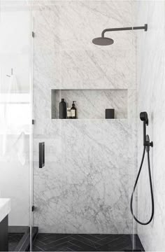 a bathroom with white marble walls and black flooring, shower head is on the wall