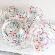 three clear balloons filled with sprinkles on top of a marble countertop