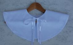 a white blouse with a bow on the front and tie around the neck, hanging on a wooden hanger