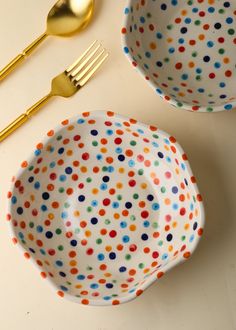 two polka dot bowls with gold forks and spoons next to each other on a table