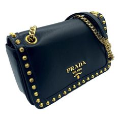 This show stopping Prada crossbody bag is crafted from black calf leather and is adorned with gold studs on the front face, along with the iconic logo plaque. The black jacquard-lined interior is conveniently equipped with a slip and zipper pocket for organizing your essentials in style. Versatile and fashion forward, this handbag features a sliding gold chain and leather strap that can be worn as a crossbody or shoulder bag. Effortlessly transition from day to night styles with this sophisticat Prada Bag Saffiano, Studded Bag, Front Face, Prada Crossbody, Iconic Logo, Luxury Packaging, Chain Crossbody Bag, Prada Crossbody Bag, Black Bag