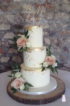 a three tiered wedding cake with pink flowers and greenery sits on a wood slice