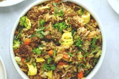 a white bowl filled with rice, meat and veggies on top of a table