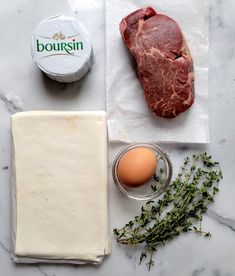 raw meat, eggs and butter on a marble counter top with napkins next to it