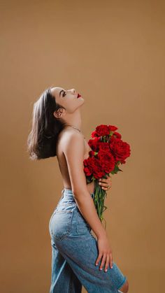 a woman is holding a bouquet of red roses in her right hand and looking up at the sky