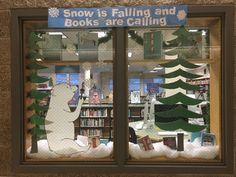 there is a window decorated with snow and trees in the store front, which reads snow is falling and books are calling