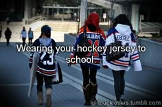 three girls are walking down the street with hockey jerseys on and one girl is holding an umbrella