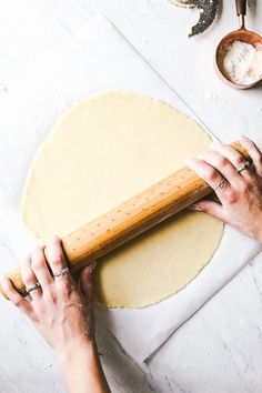 a person rolling out dough on top of a white table with wooden utensils