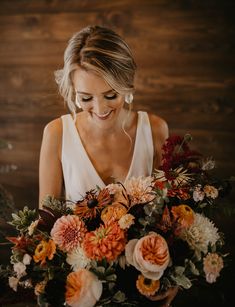 a woman holding a bouquet of flowers in front of a wooden wall and looking at the camera