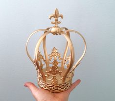 a hand holding a gold crown with filigrees