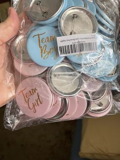 a person holding a bag full of pink and blue buttons with gold writing on them