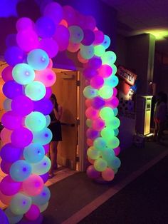 an arch made out of balloons is lit up with purple and green lights in the background